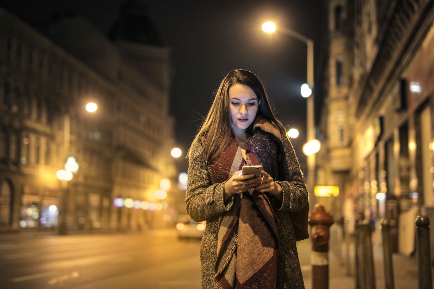 Pessoa na rua à noite, sob a luz do poste, mandando mensagem pelo celular